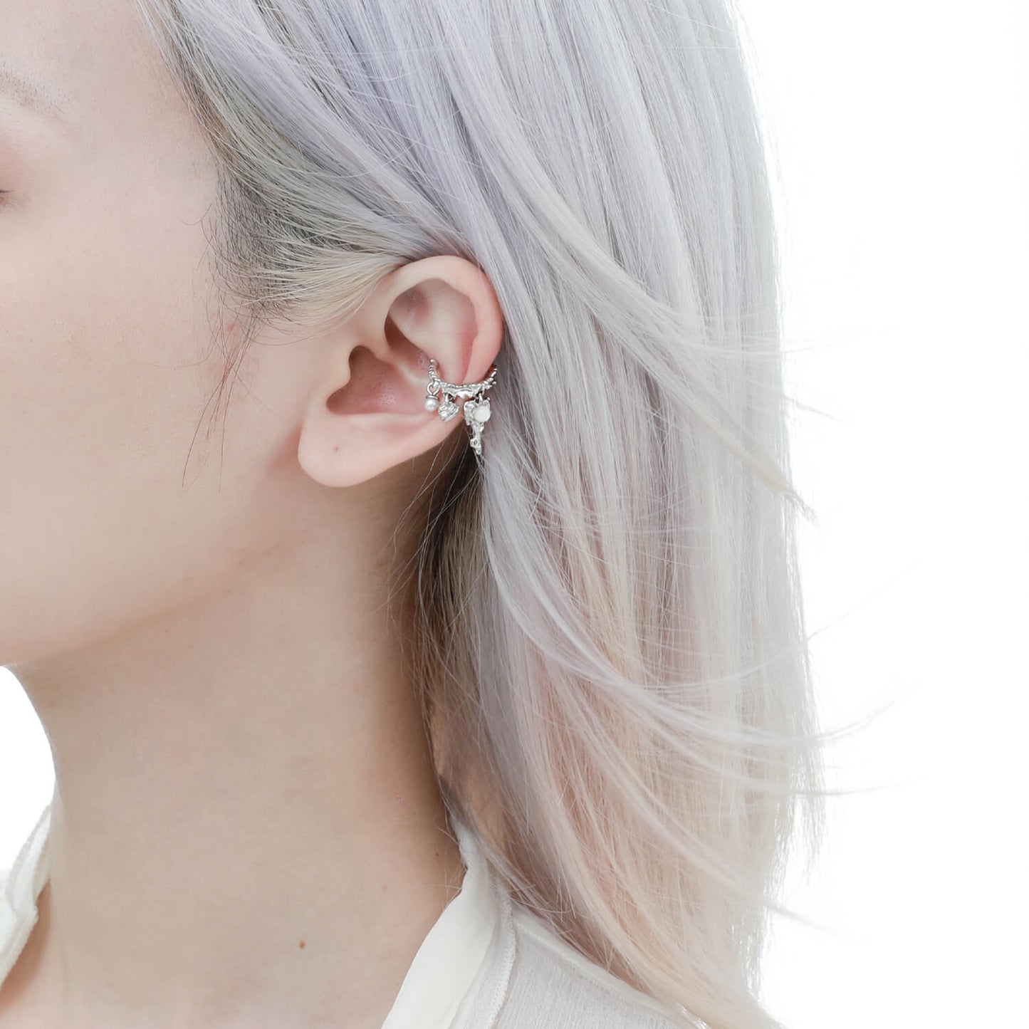 Embrace the charm of unique jewelry with these ear clips. The irregular round circles hold a trio of dainty pendants, including a delicate lock, a heart, and a lustrous pearl. The combination of these minuscule yet detailed elements adds an air of sophistication to your look.